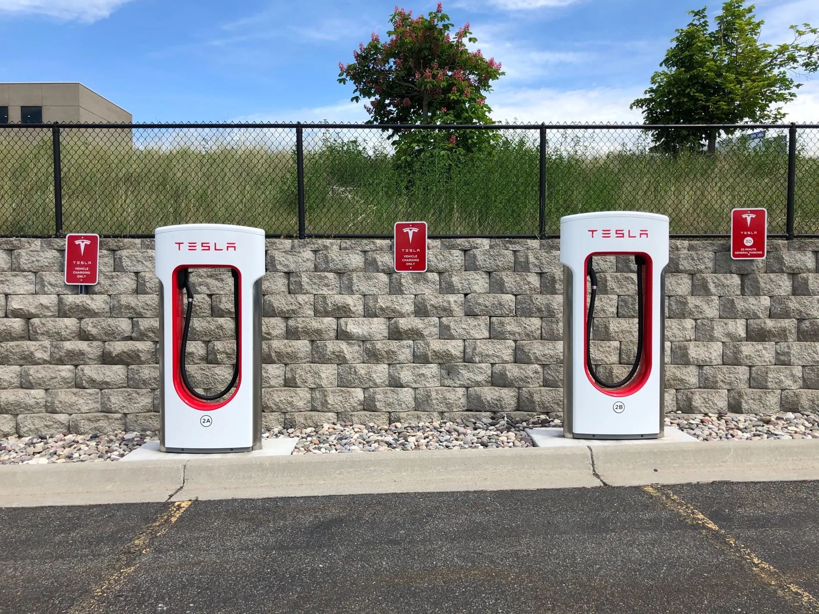Two red-and-white Tesla Superchargers at a commercial parking lot